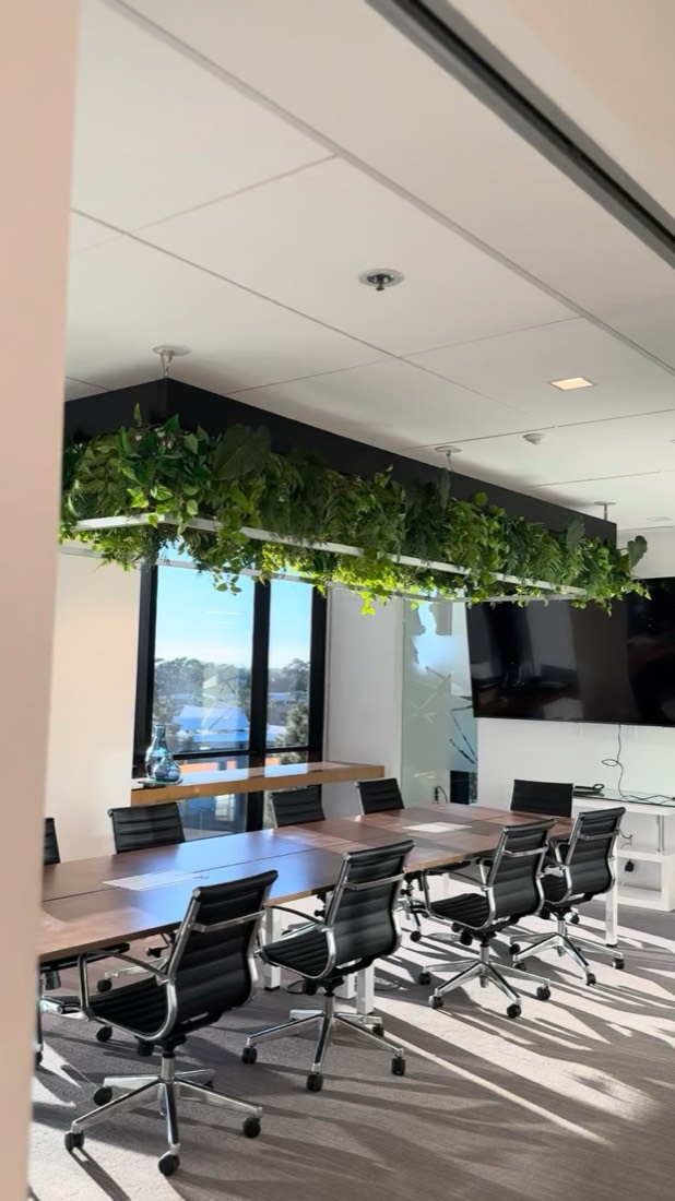 Greenery-integrated linear light fixture suspended over a conference room table, by The Plant Artist