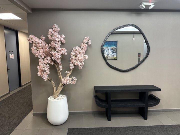 Faux cherry blossom tree in a white egg planter in an elevator lobby beside an organic mirror