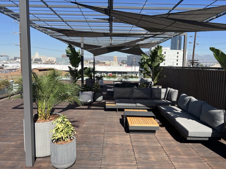 Downtown LA rooftop deck with shade sails, sectionals, and fluted planters of palms and crotons