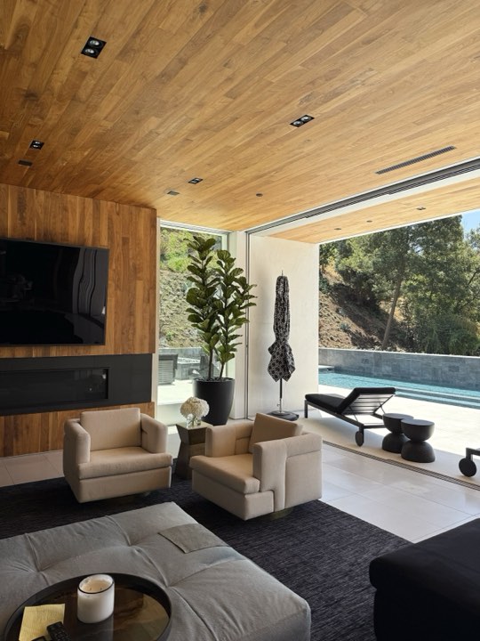 Luxury indoor-outdoor living room with wood ceiling, faux fiddle leaf fig, and pool view